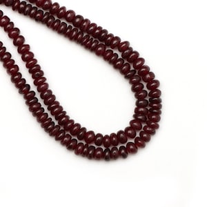 Puede incluir: Una hebra de cuentas de piedras preciosas de color rojo oscuro. Las cuentas son redondas y tienen un acabado liso y pulido.