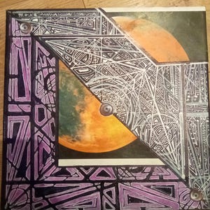 May include: A square canvas painting featuring a geometric design in black, white, and purple. The design is centred around a circular image of a planet with orange, yellow, and green hues.