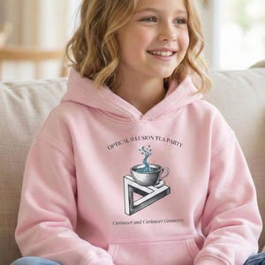 May include: A light pink hoodie with a graphic that reads "OPTICAL ILLUSION TEA PARTY" above a surreal image of a teacup and a Penrose triangle. The text "Curioser and Curioser Geometry" is below the graphic. The hoodie has a front pocket and a hood.