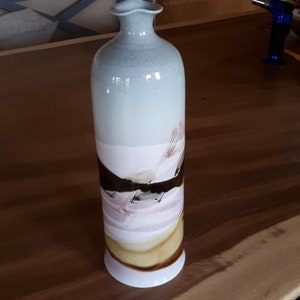 Può includere: Un vaso in ceramica bianca con una glassa macchiettata e disegni astratti marroni, rosa e gialli. Il vaso ha un fondo arrotondato e un collo stretto.