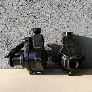 Può includere: Due coperture per prese elettriche nere di forma rotonda e superficie testurizzata. Le coperture hanno un'apertura filettata su un lato e una piccola leva sull'altro.