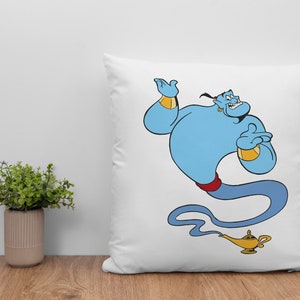 May include: White pillow with a blue genie character from the movie Aladdin. The genie is smiling and holding his hand up. He is wearing a red sash and a gold bracelet. The genie is coming out of a gold lamp.