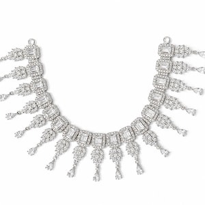 May include: A silver-toned necklace with a series of rectangular and round-cut clear stones. The necklace features dangling teardrop-shaped accents. The design is symmetrical and set against a white background.