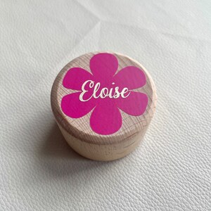 Könnte beinhalten: Eine Holzkiste mit einem rosa Blumendesign und dem Namen "Eloise" in weiß auf dem Deckel.