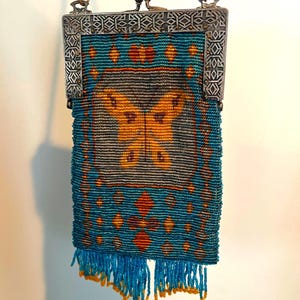 May include: Vintage beaded purse with a silver metal frame and chain. The purse features a teal and orange butterfly design, with teal beads and orange accents. The bottom has teal fringe with orange tips.