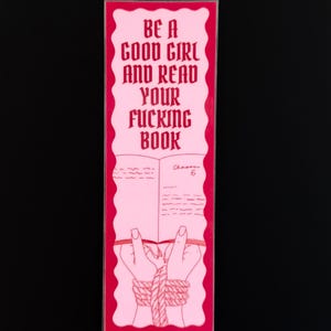 May include: Pink bookmark with red border and text that reads "BE A GOOD GIRL AND READ YOUR FUCKING BOOK". The bookmark features an illustration of a book with hands tied with rope.