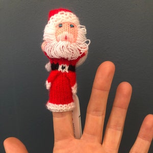 Könnte beinhalten: Eine rote und weiße gestrickte Fingerpuppe von Santa Claus mit weißem Bart und blauen Augen. Die Puppe ist auf einem Finger.