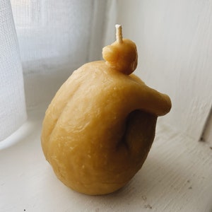 May include: A small, yellow, hand-shaped candle with a single wick. The candle is made of beeswax and has a natural, rustic look.