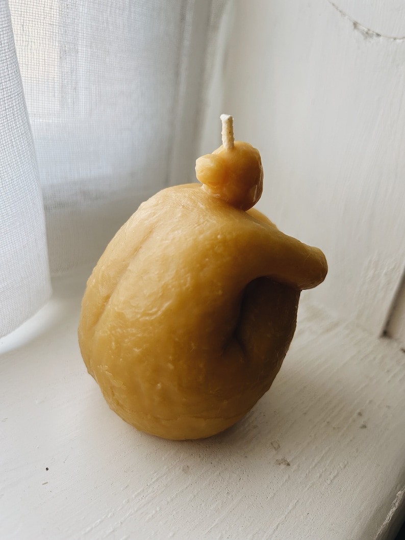 May include: A small, yellow, hand-shaped candle with a single wick. The candle is made of beeswax and has a natural, rustic look.