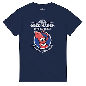 Peut inclure: Un t-shirt bleu marine à manches courtes avec un motif de calmar rouge de dessin animé dans un cercle bleu. Au-dessus du motif se trouve le texte "OBED MARSH DEVIL REEF FISHERY" avec une icône de couronne, et en dessous "Innsmouth, Massachusetts".