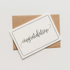 May include: A white card with a black dotted border and the word "congratulations" written in cursive.