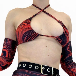 May include: A red and black marbled print bikini top with a halter neck and matching arm warmers. A black canvas belt with silver metal eyelets and buckle is worn over a matching high-waisted bikini bottom.