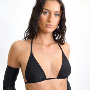 May include: A woman wearing a black halter top bikini with long black sleeves. She has long dark hair and blue eyes. She has a small infinity symbol tattoo on her chest.