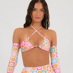 May include: A white crop top with a halter neckline and a floral pattern. The top has matching long sleeves with a floral pattern. The top is paired with a matching skirt with a floral pattern.