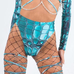 May include: Teal and black patterned high-waisted shorts with a crocodile print. The shorts are worn with black fishnet stockings and teal and black patterned garters with silver rings.