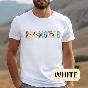 Op de afbeelding: Wit T-shirt met de tekst "PROMOTED Daddy of two" in regenboogkleuren.