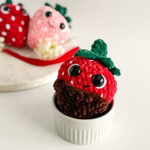 Peut inclure: Un jouet en peluche en forme de fraise crochet&eacute; avec un fond enrob&eacute; de chocolat, assis dans un bol en c&eacute;ramique blanc. La fraise a une feuille crochet&eacute; verte et des yeux en boutons noirs.