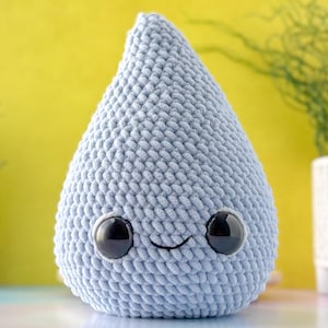 May include: A light blue crocheted raindrop plush toy with a smiling face and black eyes.
