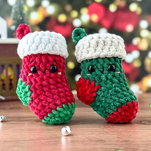 K&ouml;nnte beinhalten: Zwei handgefertigte Weihnachtsstrumpf-Ornamente. Eines ist rot mit gr&uuml;nen Akzenten, das andere ist gr&uuml;n mit roten Akzenten. Beide haben wei&szlig;e Verzierungen und kleine schwarze Augen. Diese Pl&uuml;schdekorationen sind perfekt.