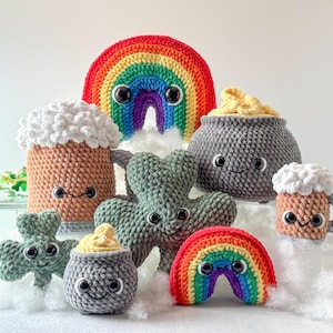 May include: A collection of crocheted amigurumi toys featuring a rainbow, a pot of gold, a beer stein, and shamrocks. The toys have cute faces and are made in various colours, including green, gold, brown, and white.