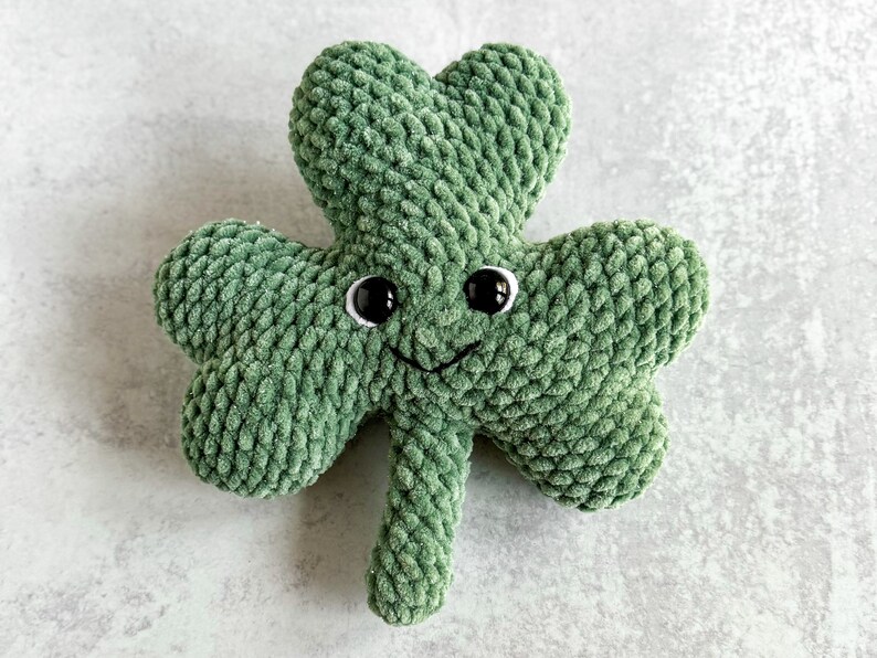 May include: A green crocheted shamrock with a smiling face and black eyes.