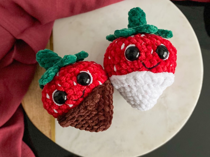 Peut inclure: Deux jouets en peluche en forme de fraise au crochet. Une fraise est rouge avec un fond en chocolat blanc et l'autre est rouge avec un fond en chocolat brun. Les deux fraises ont des feuilles vertes et des yeux noirs.