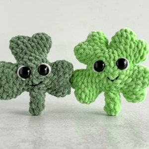 May include: Two green crocheted shamrock plush toys with black eyes and smiling faces.