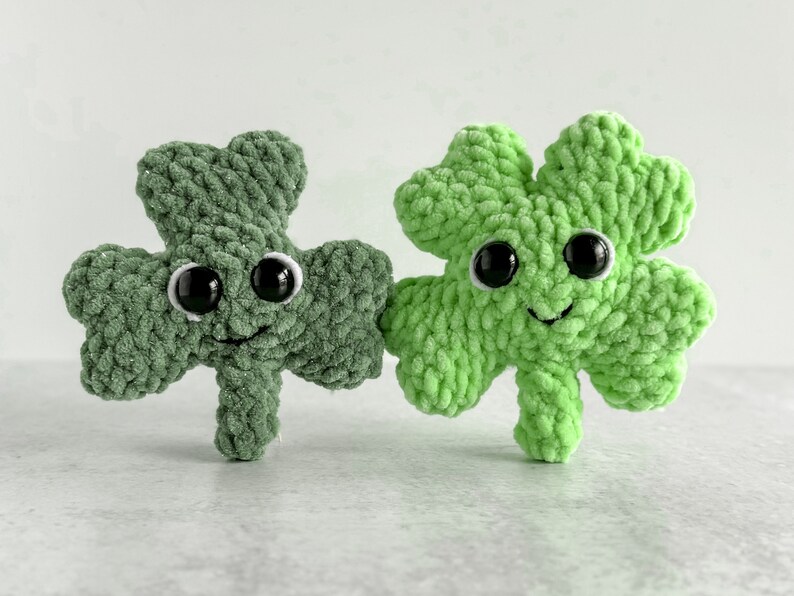 May include: Two green crocheted shamrock plush toys with black eyes and smiling faces.