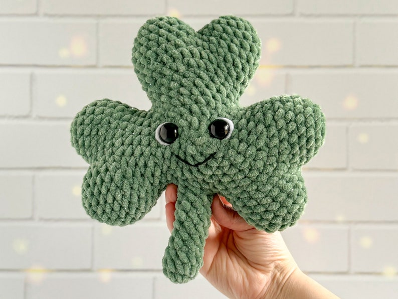 May include: A green crocheted shamrock plush toy with a smiling face and black eyes.