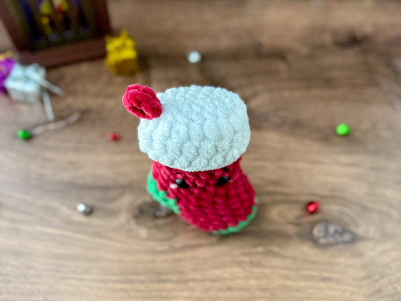 K&ouml;nnte beinhalten: Eine handgefertigte geh&auml;kelte Weihnachtsstrumpf in Rot, Wei&szlig; und Gr&uuml;n. Der Strumpf hat eine wei&szlig;e Manschette und einen roten K&ouml;rper mit gr&uuml;ner Bord&uuml;re. Ein kleiner roter Bommel ist an der Manschette befestigt. Festliche Weihnachtsdekoration.