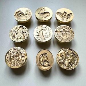 May include: Nine gold-coloured wax seal stamps featuring animal and mythical creature designs. The stamps include a squirrel, a moose, a bee, a unicorn, and a fox. Each stamp is round with a detailed relief.
