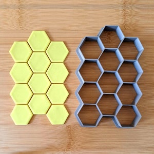 May include: A set of two honeycomb-shaped cookie cutters. The larger cutter is gray and the smaller cutter is yellow.
