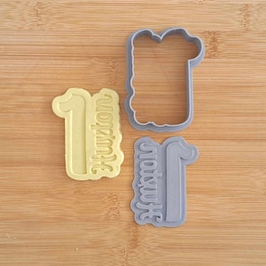 May include: Two gray plastic cookie cutters shaped like the number one with the word "Houston" written on them. One cutter is solid and the other is an outline.