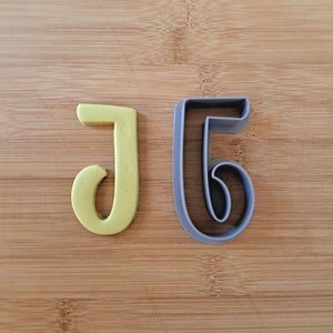 May include: A set of two cookie cutters, one shaped like the letter J and the other shaped like the number 5. The J cutter is yellow and the 5 cutter is gray.