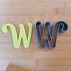 May include: A set of two cookie cutters in the shape of the letter W. The cutters are made of plastic and are in different colors. The larger cutter is gray and the smaller cutter is yellow.