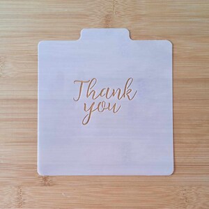 May include: White plastic stencil with the words "Thank you" in a cursive font.