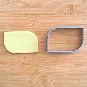 May include: A light green leaf-shaped cookie cutter and a matching cookie on a wooden surface.