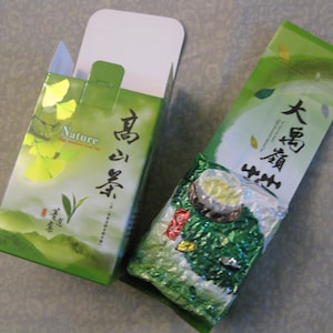 May include: A green and white tea packaging with the text "Nature" and "高山烏龍" in Chinese characters. The packaging is in a box with a white lid and a green and white design.