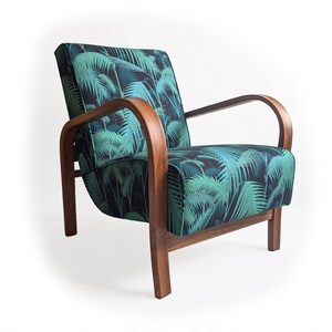 Op de afbeelding: Een houten fauteuil met een donkergroene en zwarte tropische bladmotief stoffen bekleding. De stoel heeft een gebogen houten frame en armleuningen.