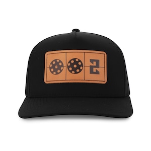 May include: Black baseball cap with a brown leather patch featuring two pickleball graphics and the number 2. The cap has a curved brim and a structured crown, suitable for outdoor activities.