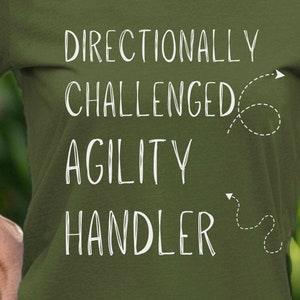 May include: A green t-shirt with the text "Directionally Challenged Agility Handler" in white. The text is accompanied by a small arrow graphic.