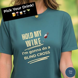 May include: Teal t-shirt with the text "HOLD MY WINE I'm gonna do a BLIND CROSS". The shirt also features a wine glass graphic and the phrase "Pick Your Drink!" with drink icons.