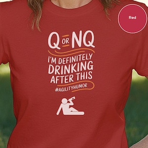 May include: Red t-shirt with a white graphic that says "Q or NQ I'm definitely drinking after this #agilityhumor". The graphic also includes a white silhouette of a person sitting down and drinking from a bottle.