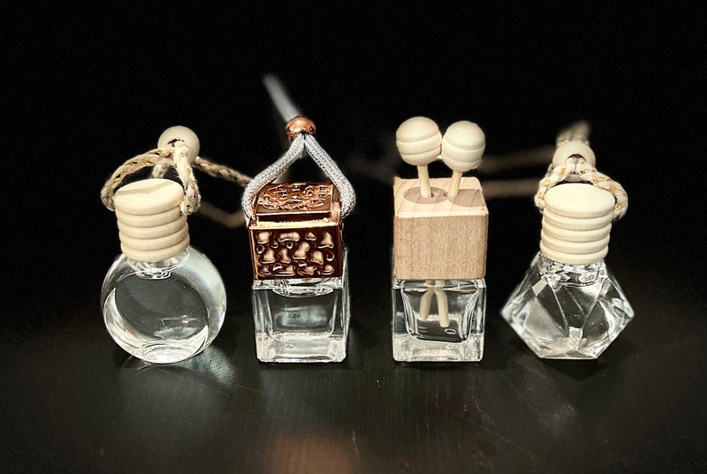 Peut inclure: Quatre diffuseurs d'air pour voiture de formes et de styles diff&eacute;rents. Les diffuseurs sont tous en verre transparent avec un bouchon blanc et une ficelle pour les suspendre. Deux des diffuseurs ont un dessus en bois, l'un a un dessus en m&eacute;tal et l'autre a un dessus rond blanc.