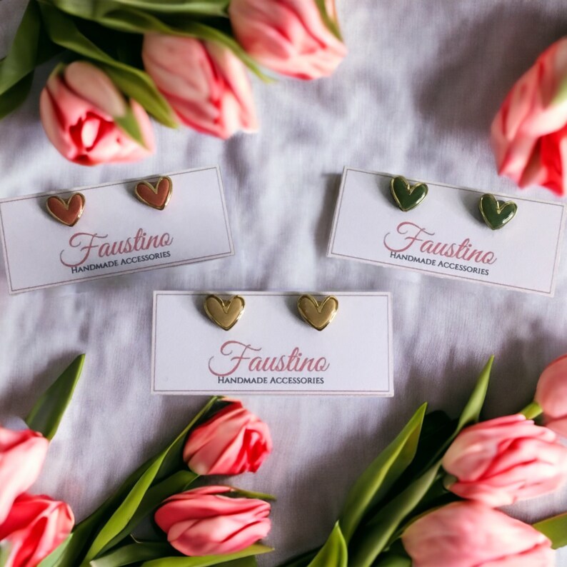 May include: Three pairs of heart-shaped earrings on white cards with the text "Faustino Handmade Accessories". The earrings are gold with pink, green, and gold enamel.