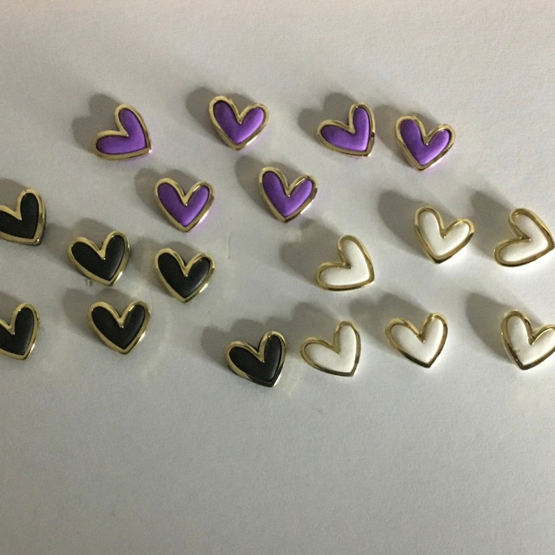 May include: Assortment of heart-shaped buttons in purple, black, and white with gold trim.