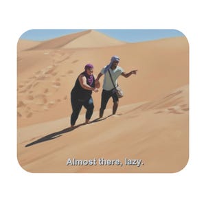 May include: A square coaster featuring an illustration of two people walking up a sand dune in a desert landscape. The text "Almost there, lazy" is at the bottom. The sky is blue.