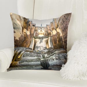 May include: A throw pillow featuring a large, weathered stone Buddha statue sitting in meditation pose. The statue is set against a backdrop of crumbling stone walls and appears to be in a temple or ancient ruin.
