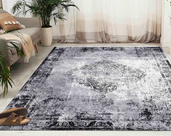 Pode incluir: Um tapete cinza e preto com um visual desgastado e vintage. O tapete tem um grande padrão intrincado no centro e uma borda ao redor das bordas.