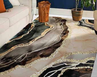 May include: Area rug with an abstract design in shades of black, brown, and beige, accented with gold-colored lines and borders. The rug has a marble-like pattern, adding a touch of elegance to any room.